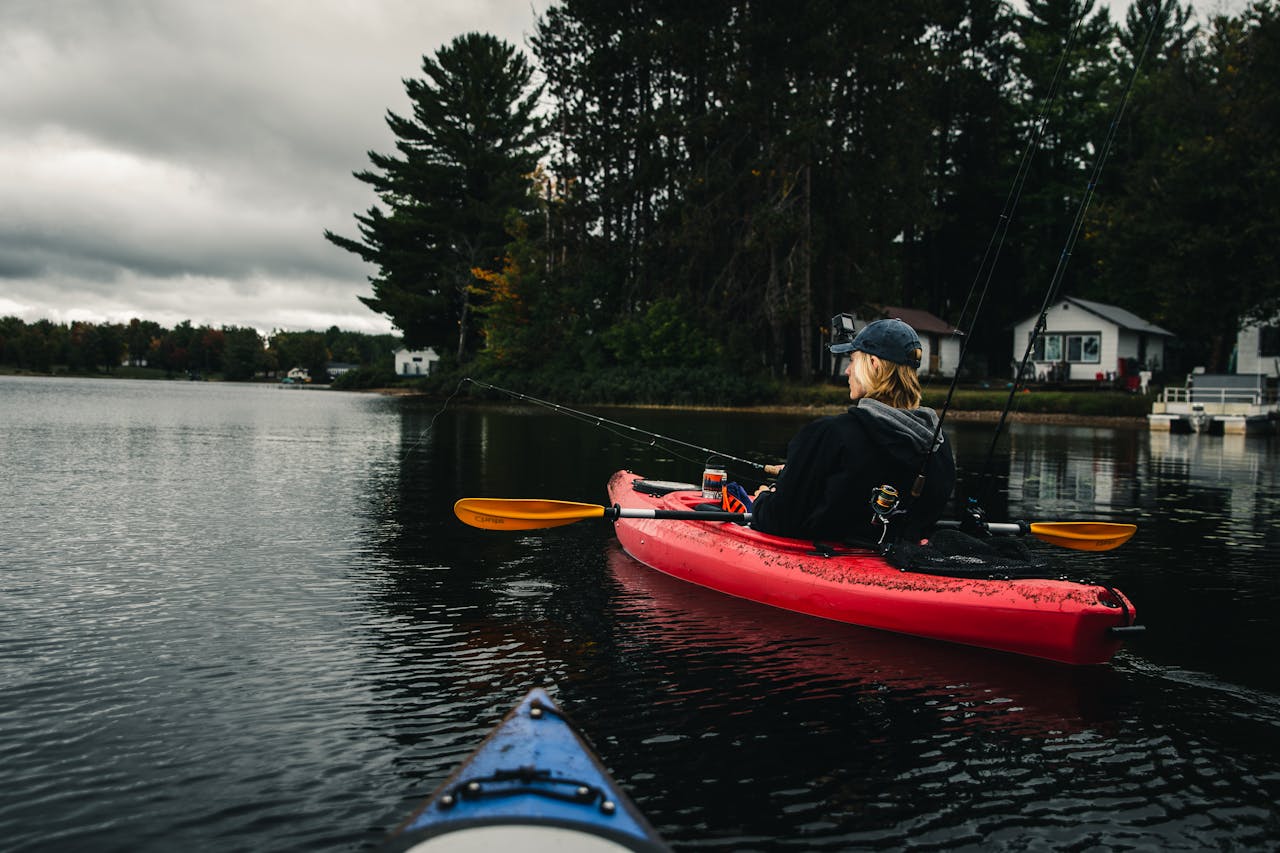 Best Fishing Kayaks for Beginners A person in a red kayak fishing on a serene lake under a cloudy sky.